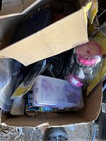 Photo of a cardboard box containing assorted tools, hardware, paintbrushes, and an unused respirator in packaging.