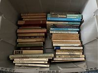 Overhead photo showing the full lot with two distinct stacks of old hardcover books, some large art poster books visible, titles partially readable such as The Hobbit and Paris