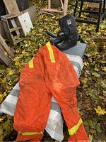 Photo showing XL insulated orange overalls with yellow reflective tape laid out, appearing used and dirty, on outdoor surface covered with leaves.