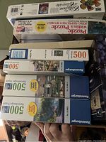 Photo showing multiple puzzle boxes stacked, including Whitman King Neptune's World with 1000 pieces, and three Ravensburger 500 piece puzzles with various scenic themes.