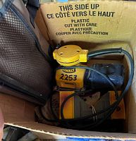Photo showing yellow and black DeWALT 1/4 sheet sander inside a cardboard box with power cord and sandpaper pieces.