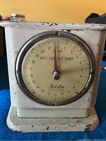 Front view of the vintage Arista mechanical scale showing the dial with weight in pounds and needle at zero, marked 'Not Legal for Trade'. The base and casing exhibit wear and rust.