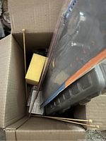 Knitting needles, sponge, plastic grids, and small boxes packed inside a cardboard box