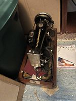 Full view of the antique Singer portable sewing machine in wooden case with black and gold details, showing machine from above.