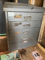 Photo of a gray metal cabinet featuring four drawers and a slanted top. Shows wear and tear with scratches and rust spots.