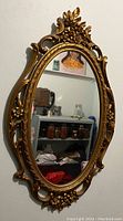 Full view of the vintage oval wall mirror with ornate gold frame mounted on white wall.