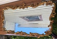 Full view of a large rectangular vintage mirror with gold ornate scrolling frame with some wear and repair marks.