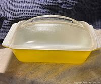 Yellow Pyrex loaf pan with clear lid sitting on fabric surface.