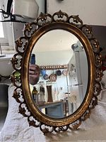 Photo of an oval vintage mirror with intricate gold-colored frame displaying kitchen reflected in mirror.