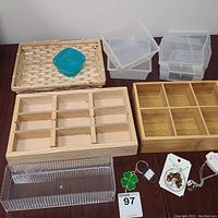 Image showing two wooden compartment boxes, four clear plastic slatwall display boxes, wicker basket with blue container inside, clear acrylic organizer box, and assorted jewelry including necklaces and keychain.