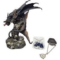 Photo showing dark black and grey dragon statue surrounded by skulls and bones with the two Celtic necklaces placed beside it