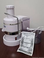 Jack LaLanne's Power Juicer unit with clear juice container and operating manual placed beside it on a flat surface.