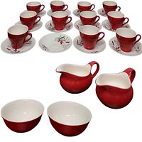 Eleven red and white teacups with matching saucers, two red milk server pitchers, and two red bowls arranged together.