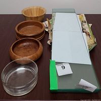 Photo showing 3 wooden bowls and 1 glass bowl aligned next to five stacked beveled glass shelves wrapped partially in newspaper.