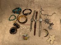 Various bracelets, watches, brooches, and pins laid out on a beige cloth background.