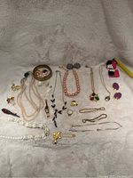 Full layout of the costume jewelry lot on a white textured surface showing various necklaces, pins, rings, bracelets, and earrings.