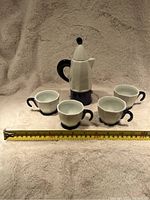 Front view of the Bialetti Moka Express pot size and four demitasse cups arranged with a measuring tape at the base showing approximate size.