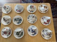Overview of 11 fine bone china teacups and matching saucers displayed on table, showing various floral patterns.