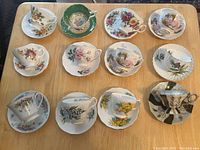 Top-down view of all 11 bone china tea cups with matching saucers in various floral and decorative patterns on a wooden table