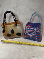 Two glass vases shaped like purses, placed next to a measuring tape showing approximately 10 inches in length for size reference.
