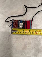 Huge white baroque pearl pendant shown on a colorful woven cloth with measuring tape indicating size.