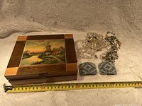 Closed wooden jewelry box with landscape painting, jewelry displayed in front showing two pairs of bead earrings and beaded necklaces. Measuring tape indicates box width approximately 25 cm.