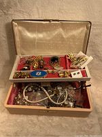 Open vintage jewelry box showing multiple pieces of costume jewelry in the red velvet tray and main compartment