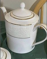 Close-up of teapot with lid, white porcelain, gold trim, embossed floral pattern