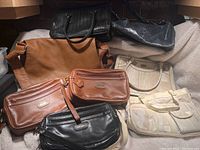 Lot showing 7 leather bags in different styles and colors laid on white fabric