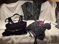 Three lingerie pieces including black leather corset, black velvet bustier, and black mesh polka dot set on cream background.