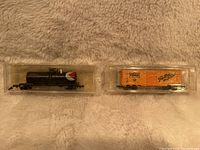 Two N scale model train cars in plastic cases: one black CP Rail tanker and one Stroh's boxcar.