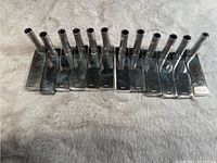 Top view of 12 silver tone Cartier name place card holders arranged in a line on a soft textured surface.