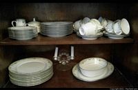 Photo showing china plates, cups, and saucers arranged on shelves in a cabinet.