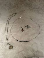 Two 925 silver necklaces and two pendants laid on a light fuzzy surface. One necklace has a round Scorpio symbol pendant. Two extra pendants (silver airplane and amber-colored stone) are between the necklaces.