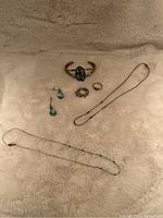 Photo of an assortment of silver and turquoise jewelry pieces on a light surface including necklaces, cuff bracelet, earrings, and rings