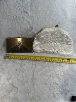Two vintage bags on a light textured surface with measuring tape showing sizes. Metal clutch has a sunburst pattern and rhinestone accent, white purse has beaded floral design.