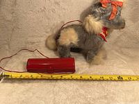Full side view of the vintage plush toy dog with attached remote and measuring tape showing length around 9 inches.