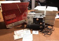 Eumig Mark 607 D 8mm projector with original box, plastic film reels, and power cord on table