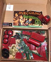 Photo showing various red, green, and black metal Meccano construction parts including wheels, gears, plates, and a red motor in a box