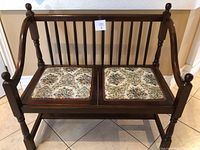 Front view of antique wooden bench showing dark wood and two removable floral upholstered seat cushions