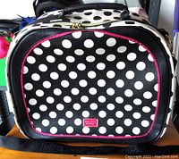Front view of black and white polka dot suitcase with pink trim and Betsey Johnson logo plate