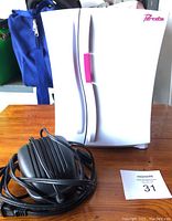 White Bratz mini fridge closed, showing pink handle and logo with power cord and instruction manual nearby.