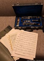 Classical clarinet disassembled and placed inside blue velvet-lined hard case with sheet music arranged beside it