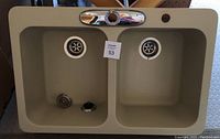 Top view of beige/tan quartz composite double bowl kitchen sink with two drain strainers and faucet hole.