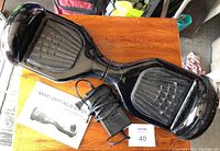 Top view of the black hoverboard with power cord and user manual on wooden table.