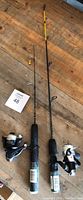 Photo of two ice fishing rods with spinning reels on wooden floor, one rod tip yellow, partially wrapped handles.