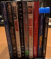 Movies DVDs and Blu-rays in cases displayed upright showing titles on spine including Yes Man, Robin Hood, Oceans Twelve, Heat, Dracula, John Candy Comedy Favourites, Toy Story 3, Unknown.