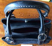 Top view of bag showing black leather handles with silver rings and zippered main compartment.