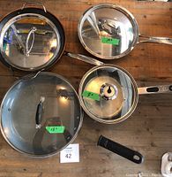 Top view of four stainless steel pots and pans with glass lids on a wooden surface