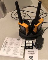 Two Uniden two-way radios seated in charging dock alongside rechargeable battery pack, power adapter, and manual on table